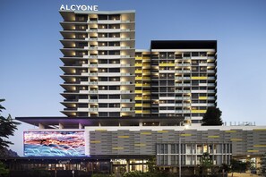 A modern hotel with multiple balconies, a prominent digital display, and a clear sky. - Alcyone Hotel Residences (Hamilton)