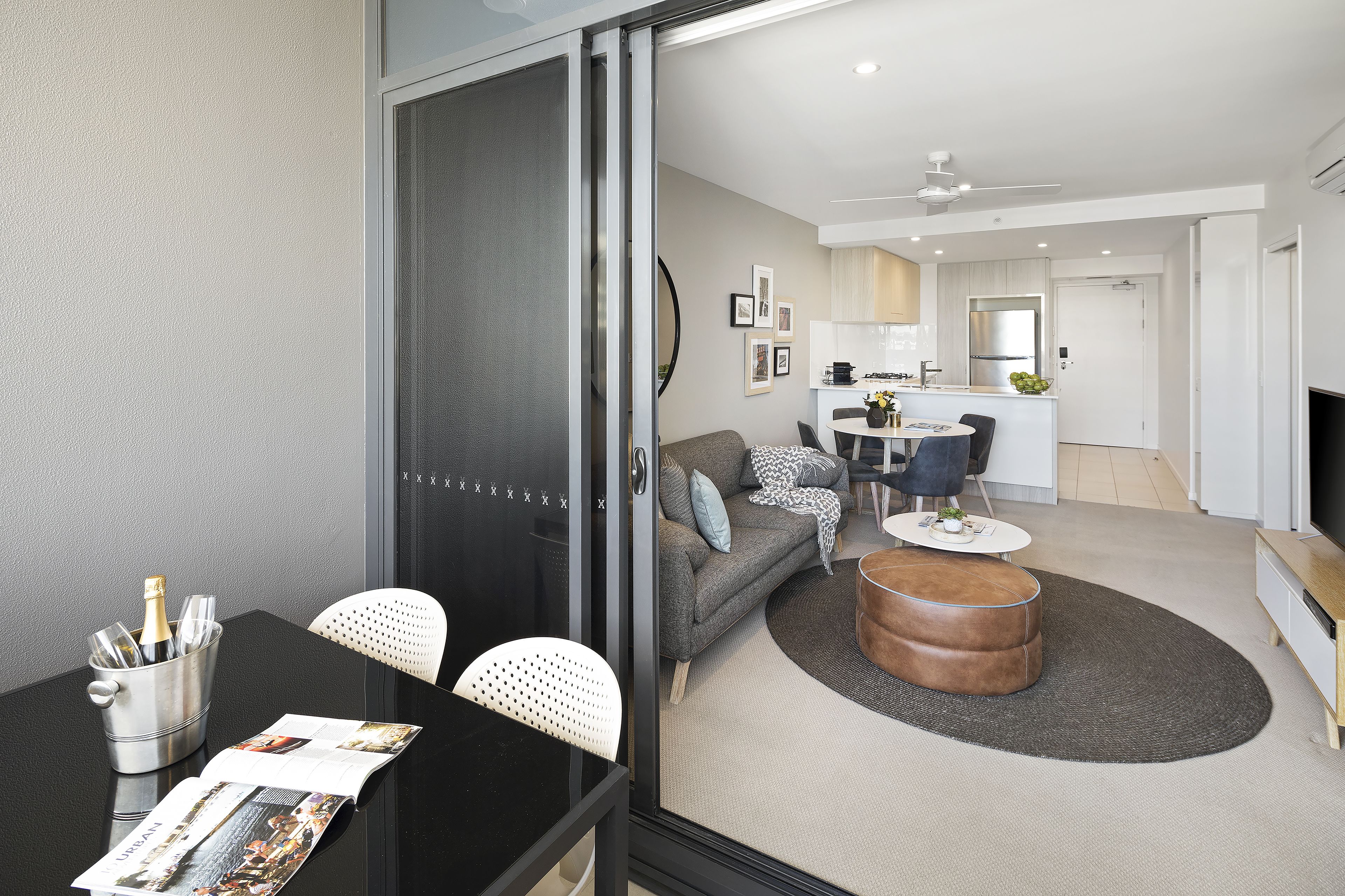 Een moderne woonkamer met een zwarte eettafel, witte stoelen, een grijze bank en een bruin voetenbankje.