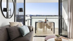 A modern living room with a sofa, a round mirror, and a dining area with two chairs and a table. - Alcyone Hotel Residences (Hamilton)