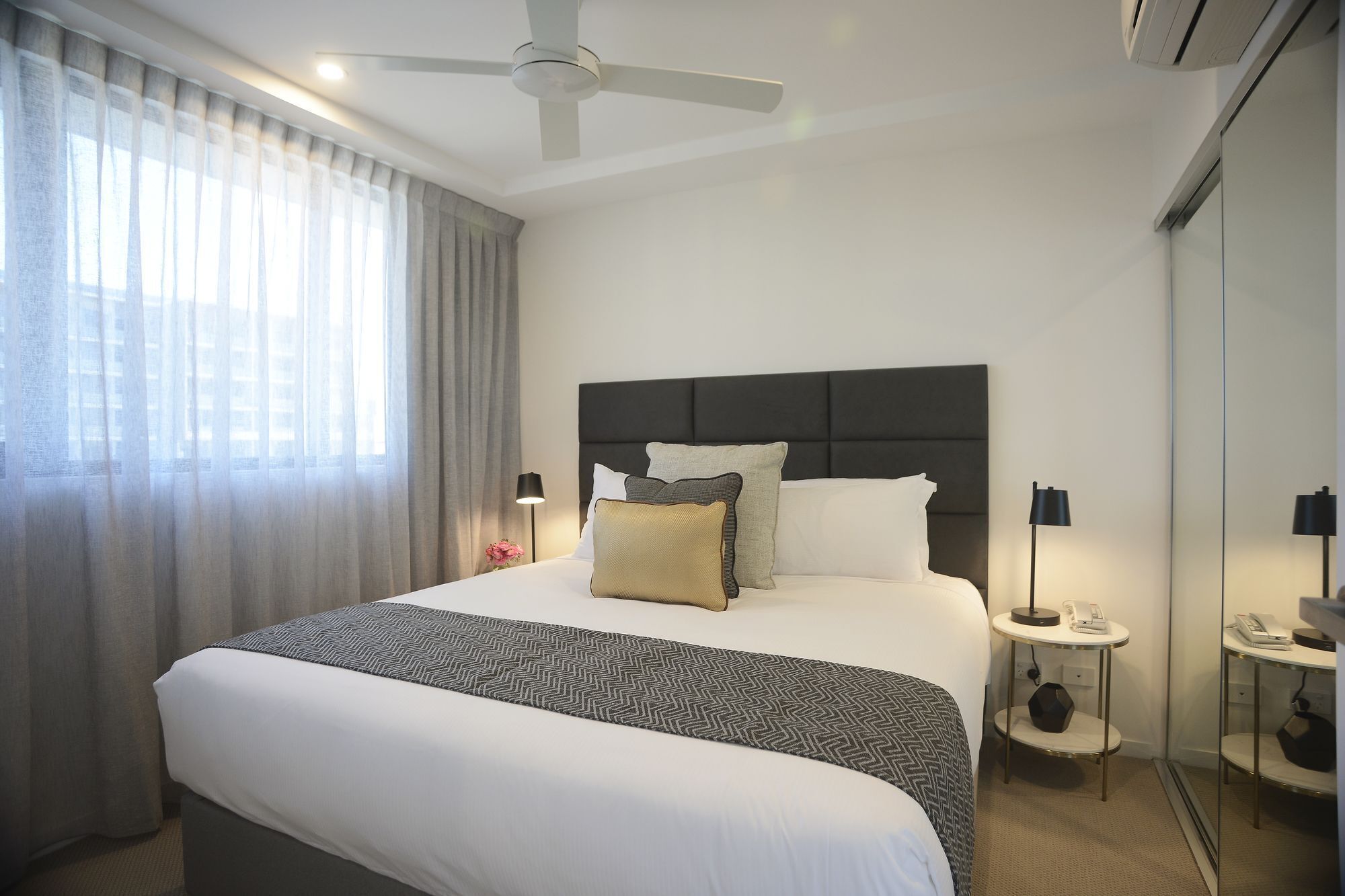 A hotel room with a large bed, a ceiling fan, a bedside table with a lamp, and a mirror.