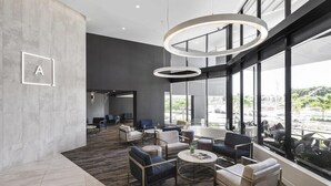 A modern lounge area with seating, a coffee table, and a large window offering a view of the city. - Alcyone Hotel Residences (Hamilton)