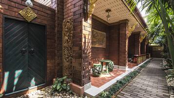 A traditional brick building with a large green door, decorative wall carvings, and a tiled patio area with outdoor furniture.