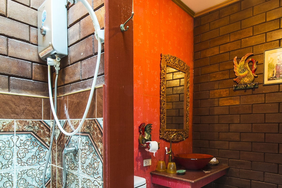 A bathroom with a shower, toilet, and sink, featuring patterned tiles and a red accent wall.