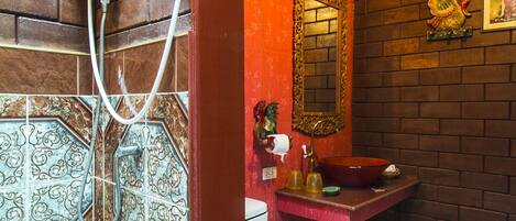 Un baño con ducha, inodoro y lavamanos, con baldosas estampadas y una pared de acento roja.