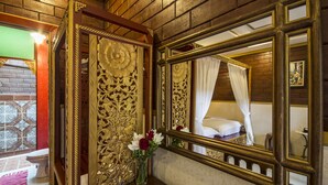 A room with a large ornate mirror, a bed with a white canopy, and a vase with flowers on a wooden table. - Irawadee Resort (Mae Sot)