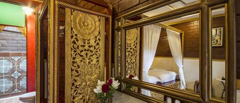 A room with a large ornate mirror, a bed with a white canopy, and a vase with flowers on a wooden table.