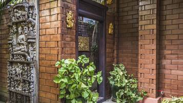 Fachada de um edifício de tijolos com uma porta de madeira escura, um relevo em baixo-relevo à esquerda e plantas em vasos à frente.