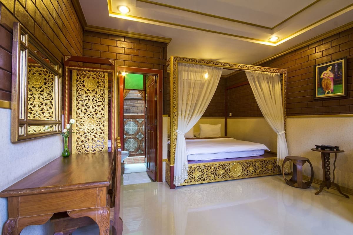 A room with a four-poster bed, a desk, a chair, and a small table.