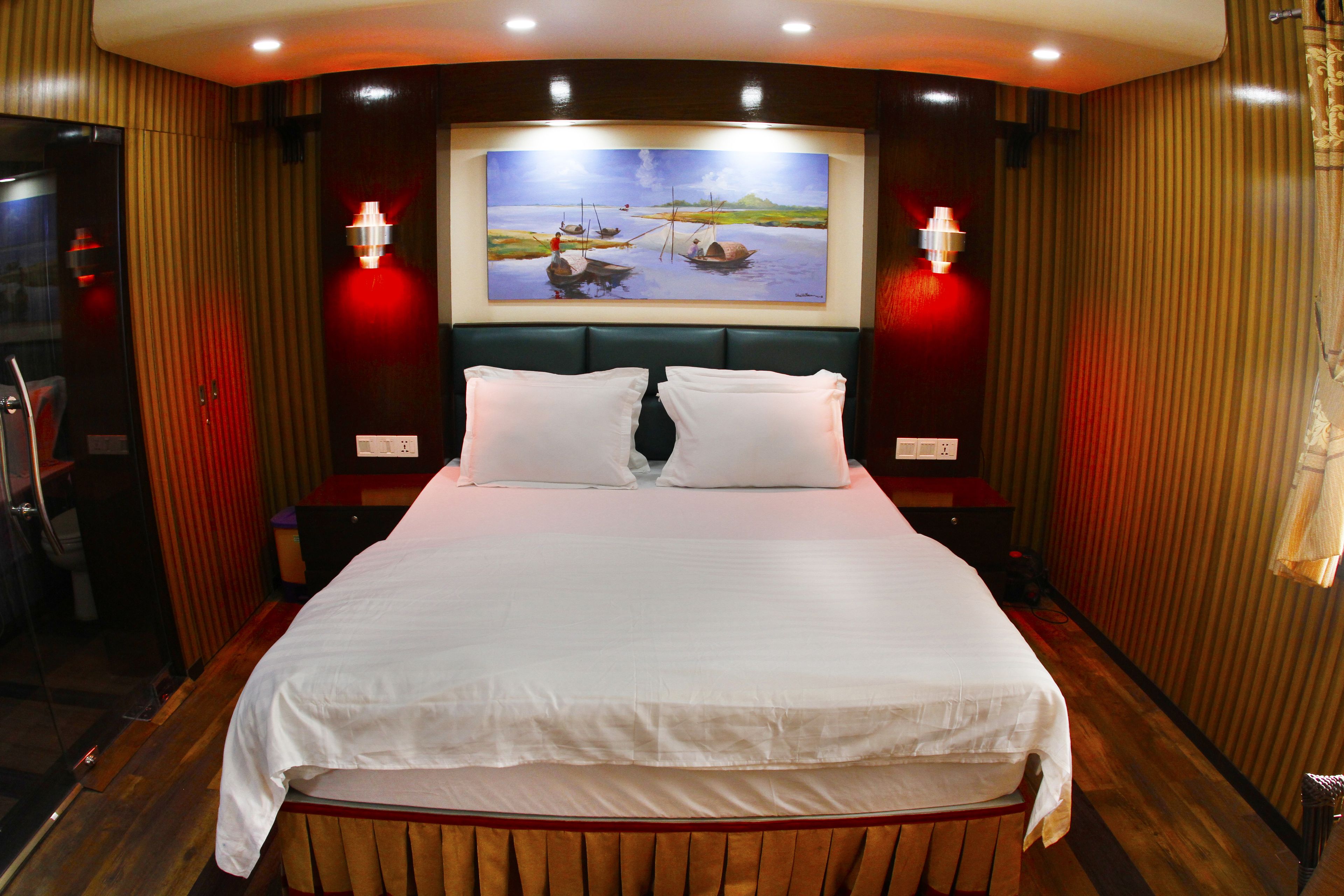 A large bed with white linens, two bedside tables, and a painting of boats on water above the bed.