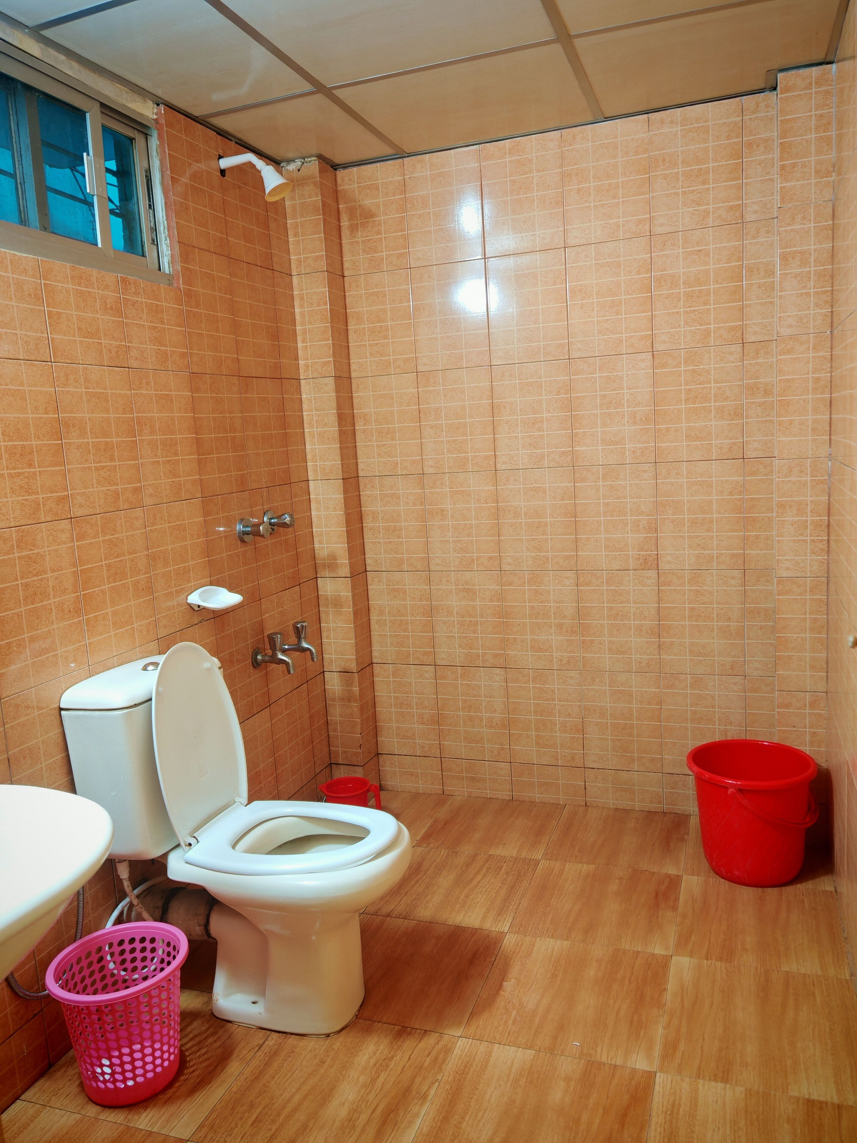 A bathroom with a toilet, a shower, and a red bucket.