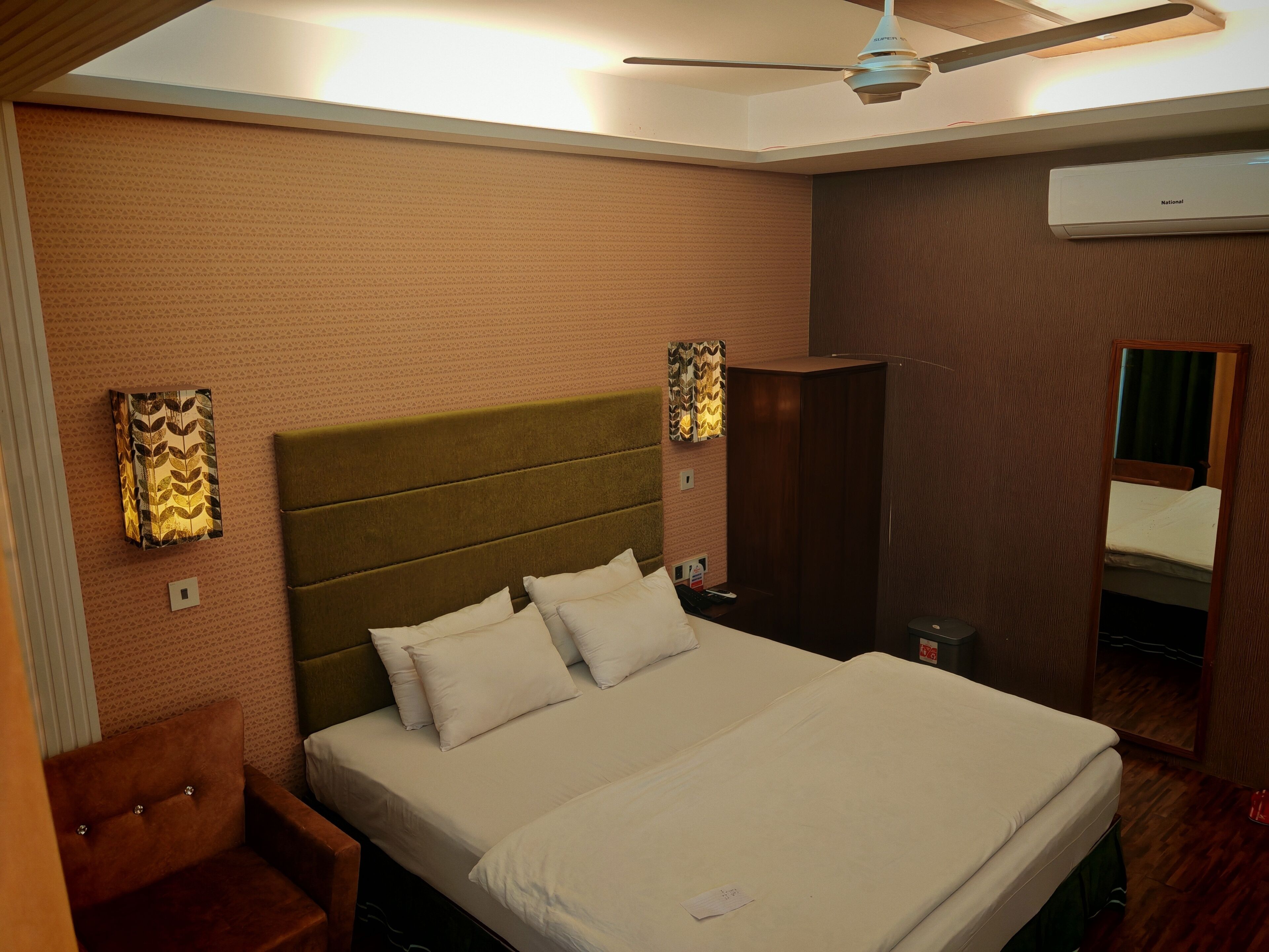 A hotel room with a large bed, a headboard, a wardrobe, a mirror, and a ceiling fan.