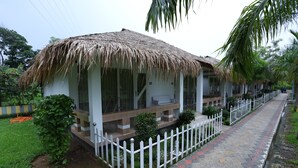 A row of thatched-roof cottages with white railings, a paved walkway, and a white picket fence. - Rangauti Resort (Moulvibazar Sadar)