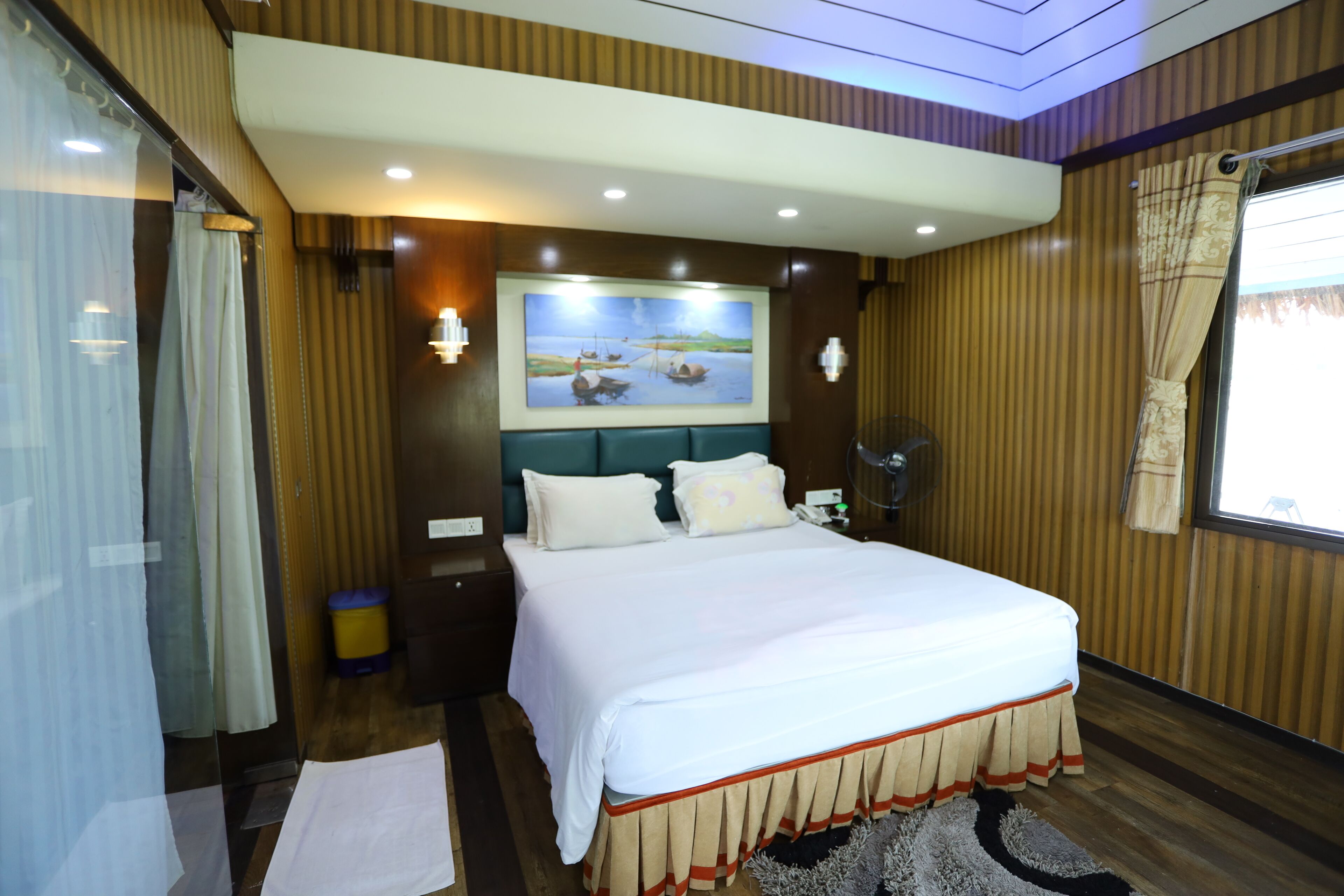 A hotel room with a large bed, a painting on the wall, and a window with curtains.