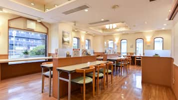 Um restaurante espaçoso com piso de madeira, várias mesas e cadeiras, e grandes janelas que oferecem vista para o exterior.