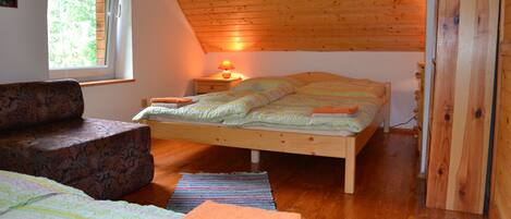 A bedroom with a sloped ceiling, a bed, a nightstand, a lamp, and a window.