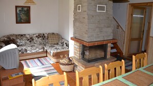 A cozy living room with a stone fireplace, a sofa, a television, and a dining table with chairs. - Chata Pohoda Slovenský Raj (Spišské Tomášovce)