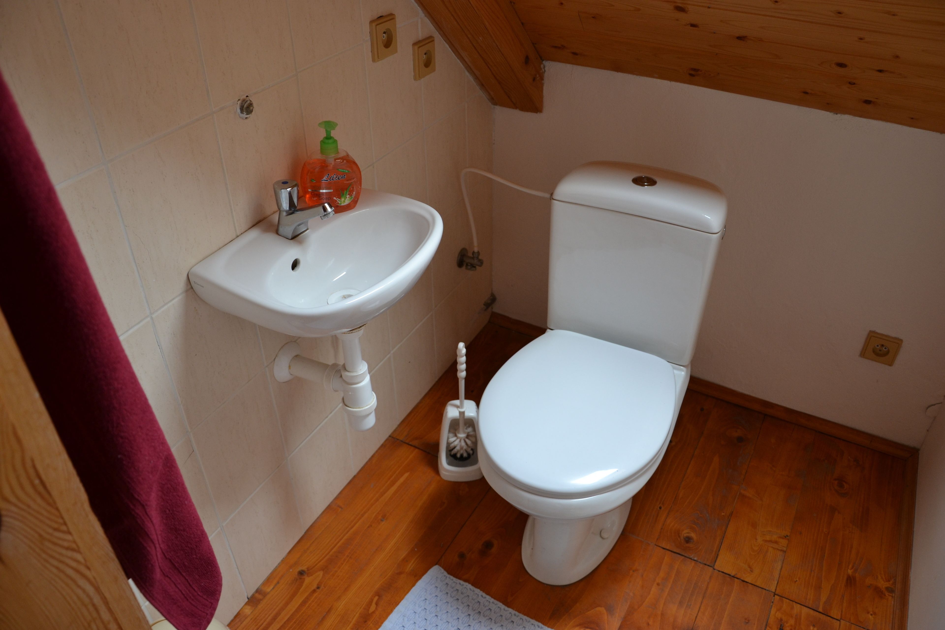 A small bathroom with a white sink, toilet, and wooden floor.