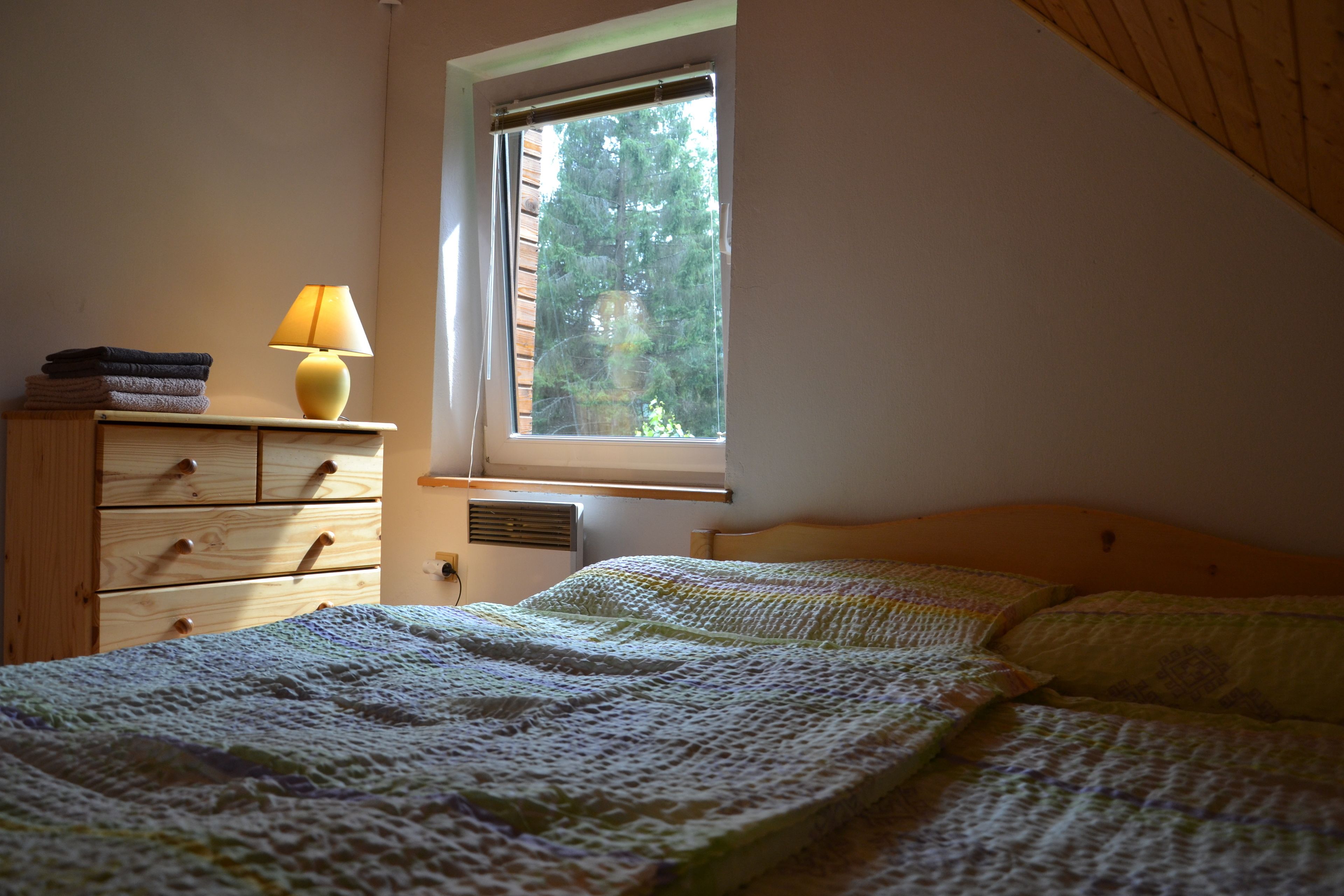 A bedroom with a bed, a dresser, a lamp, and a window with a view of trees.