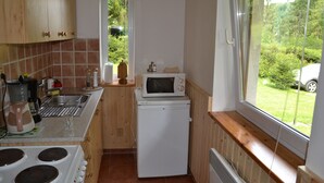 A compact kitchen with wooden cabinets, a microwave, a small refrigerator, and a window offering a view of greenery outside. - Chata Pohoda Slovenský Raj (Spišské Tomášovce)