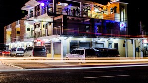 Un hôtel à plusieurs étages, doté de balcons, d’une enseigne lumineuse et d’un parking où sont garées des voitures.