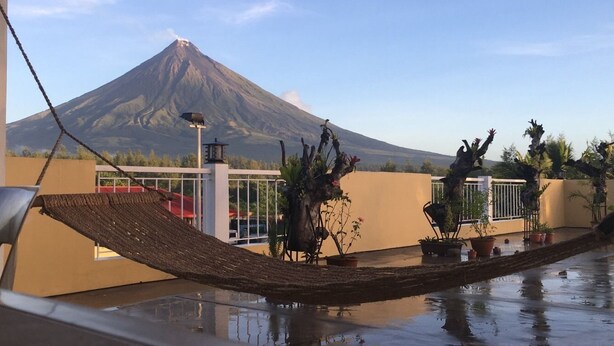 Un hamac sur un balcon donnant sur un volcan, avec des plantes en pot et un ciel dégagé.