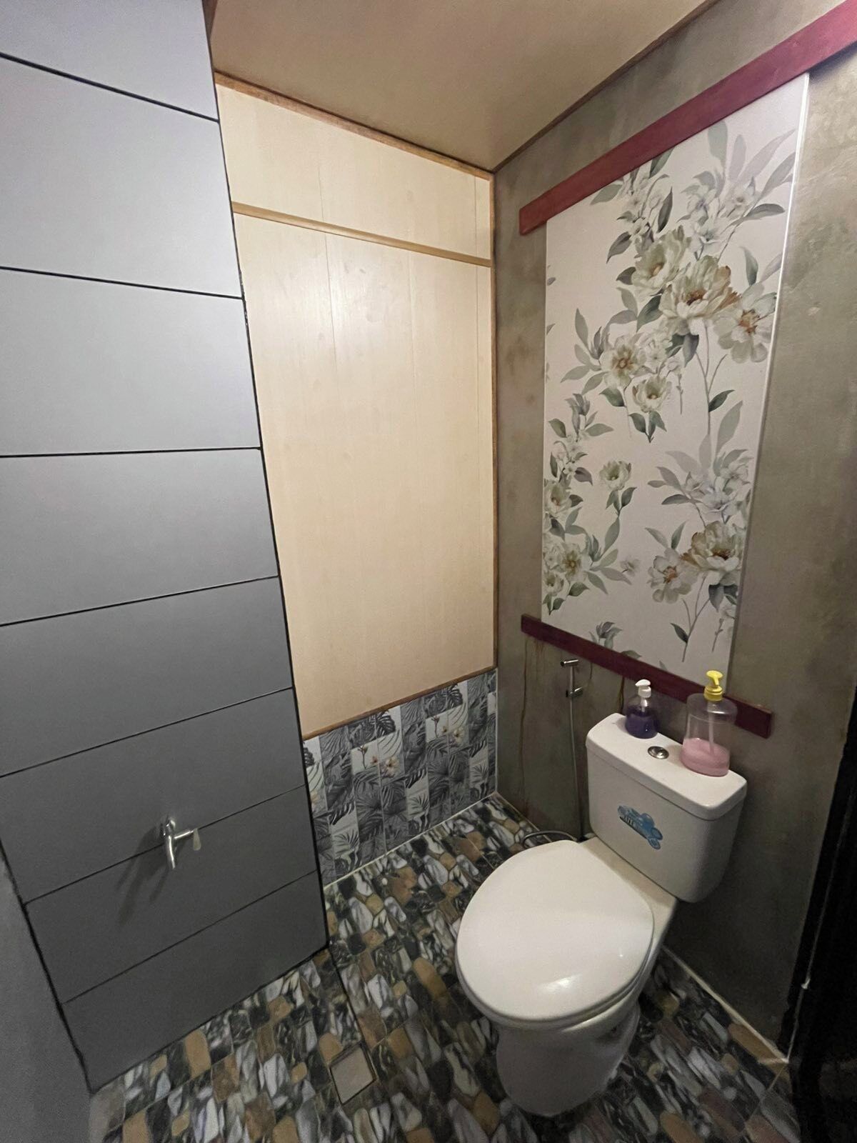 A bathroom with a toilet, a cabinet, and a decorative floral wall panel.