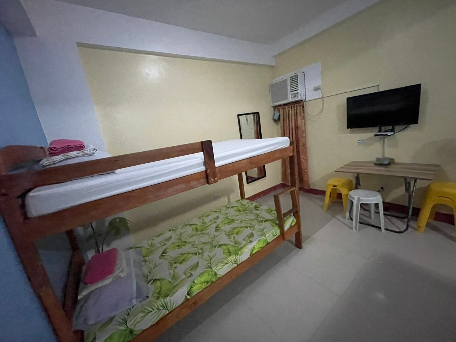 Una cama individual superpuesta con colchón, un escritorio con silla, un televisor y un equipo de aire acondicionado en una habitación.