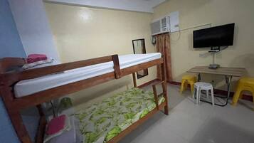 Una cama individual superpuesta con colchón, un escritorio con silla, un televisor y un equipo de aire acondicionado en una habitación.