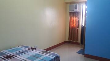 A room with a bed, a door leading to another room, and an air conditioning unit on the wall.