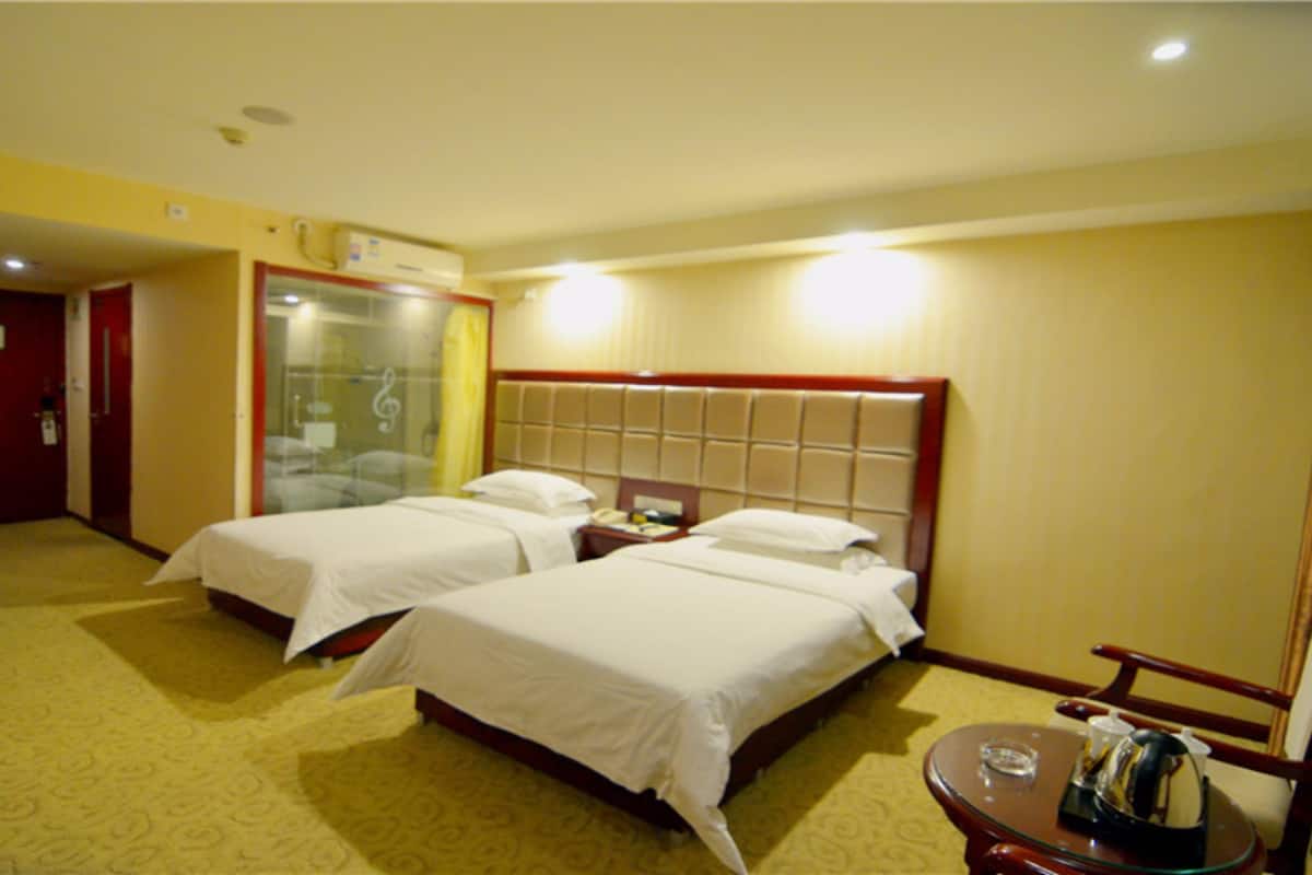 A hotel room with two beds, a small table with a kettle, and a mirror.