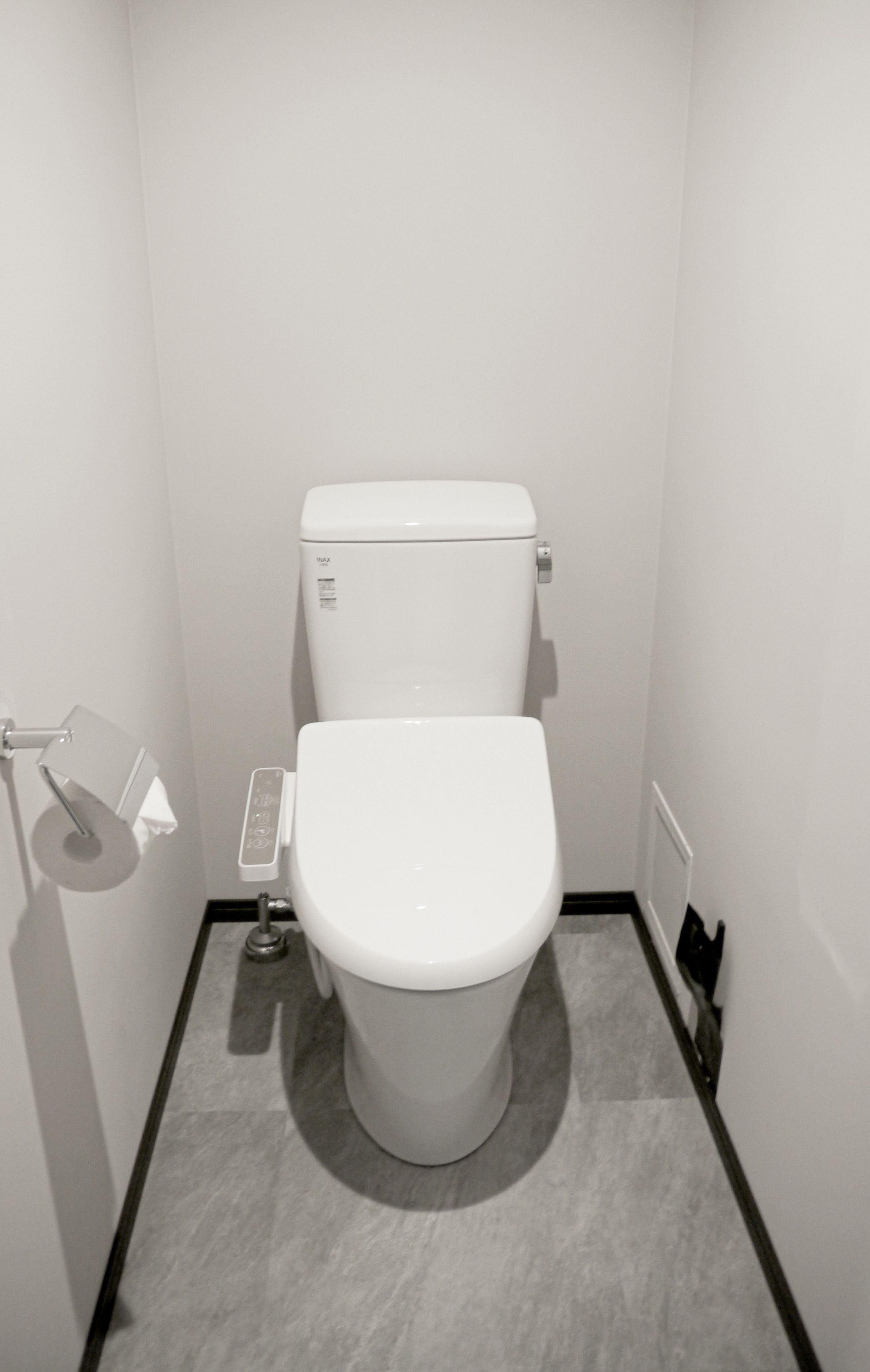 A small, white, modern bathroom with a toilet, a toilet paper holder, and a radiator.