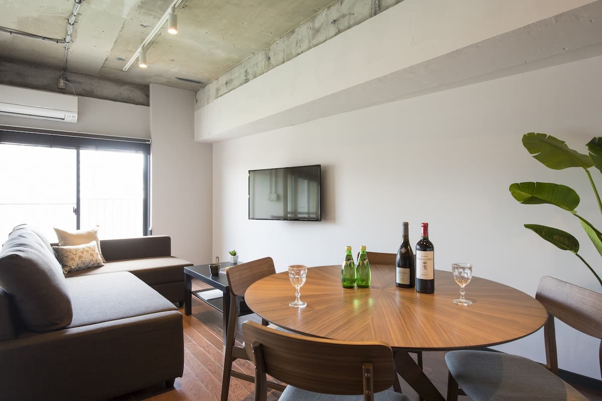A modern living room with a wooden dining table, two chairs, a sofa, and a television mounted on the wall.