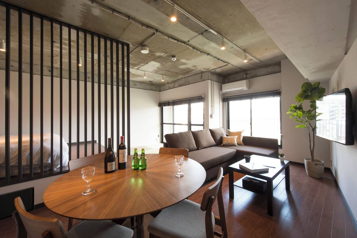 A modern interior with a round wooden table, seating, a sofa, and a large window.