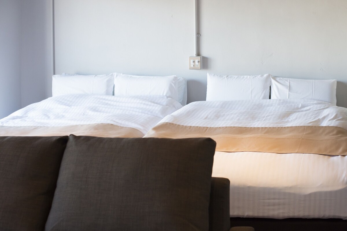 A hotel room with two beds, a nightstand, and a chair.