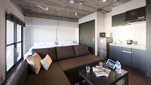 A modern hotel room with a large bed, a sofa, a small kitchen area, and a dining table with a magazine and glasses. - A Good Day Fukuoka Riverside (Fukuoka)