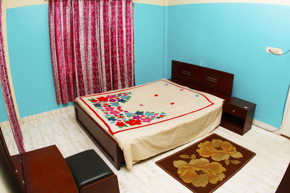 A bedroom with a bed, nightstand, dresser, and a floral rug.