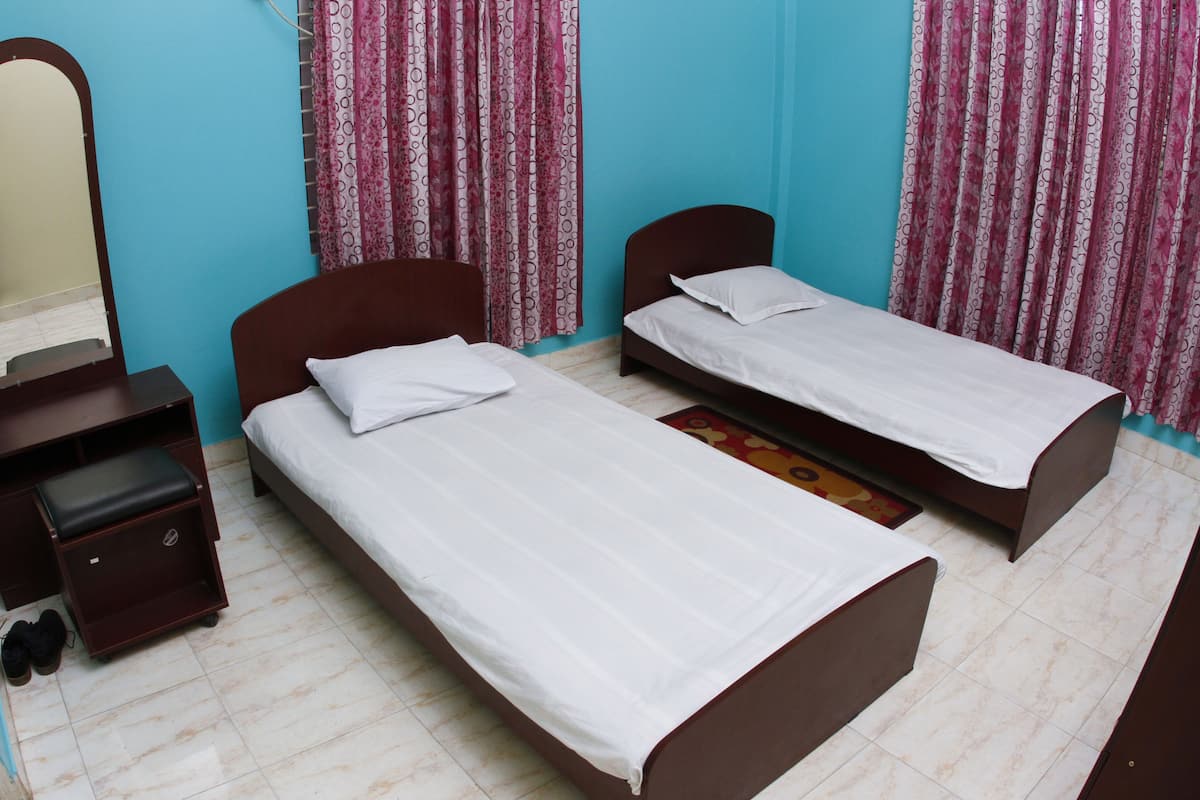 A room with two single beds, a wooden dresser, a mirror, and patterned curtains.