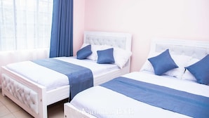 Two twin beds with white headboards and blue bedding in a room with a pink wall and a window with blue curtains.