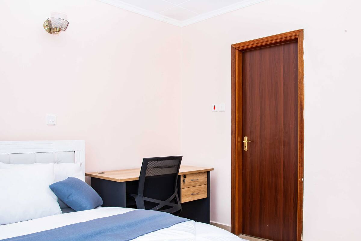 A bedroom with a bed, a desk, and a wooden door.