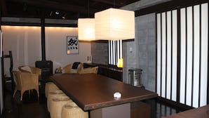 A dining area with a long wooden table, wicker chairs, a hanging light fixture, and a wall with vertical slats.