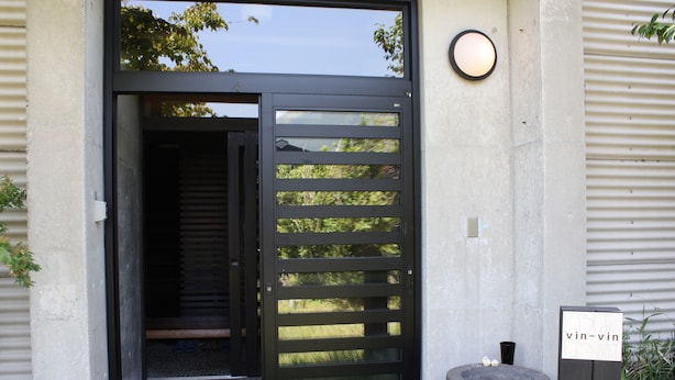 A modern entrance with a black sliding door, a stone planter with a sign, and a concrete wall.