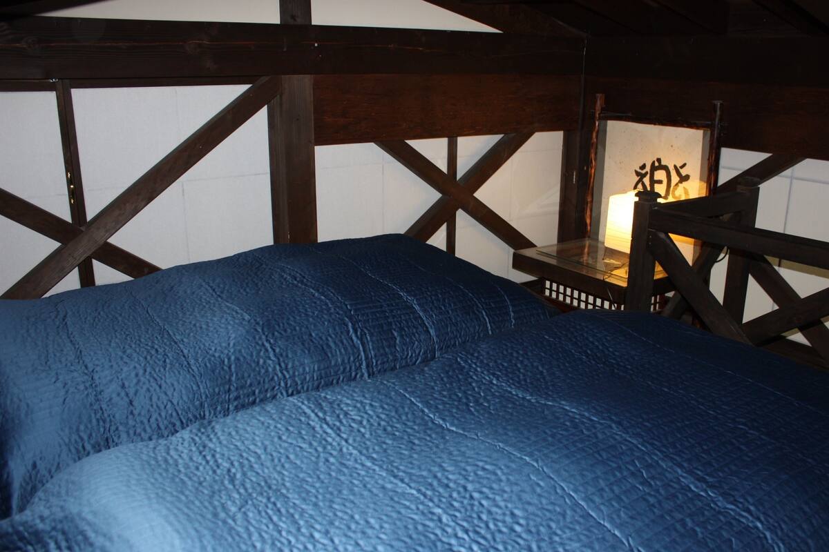 Ein Zimmer mit Bett, Holzbalken und einem Tisch mit Lampe.
