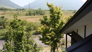 A view from a window overlooking a rural landscape with mountains in the distance, a clear sky, and a road in the foreground.