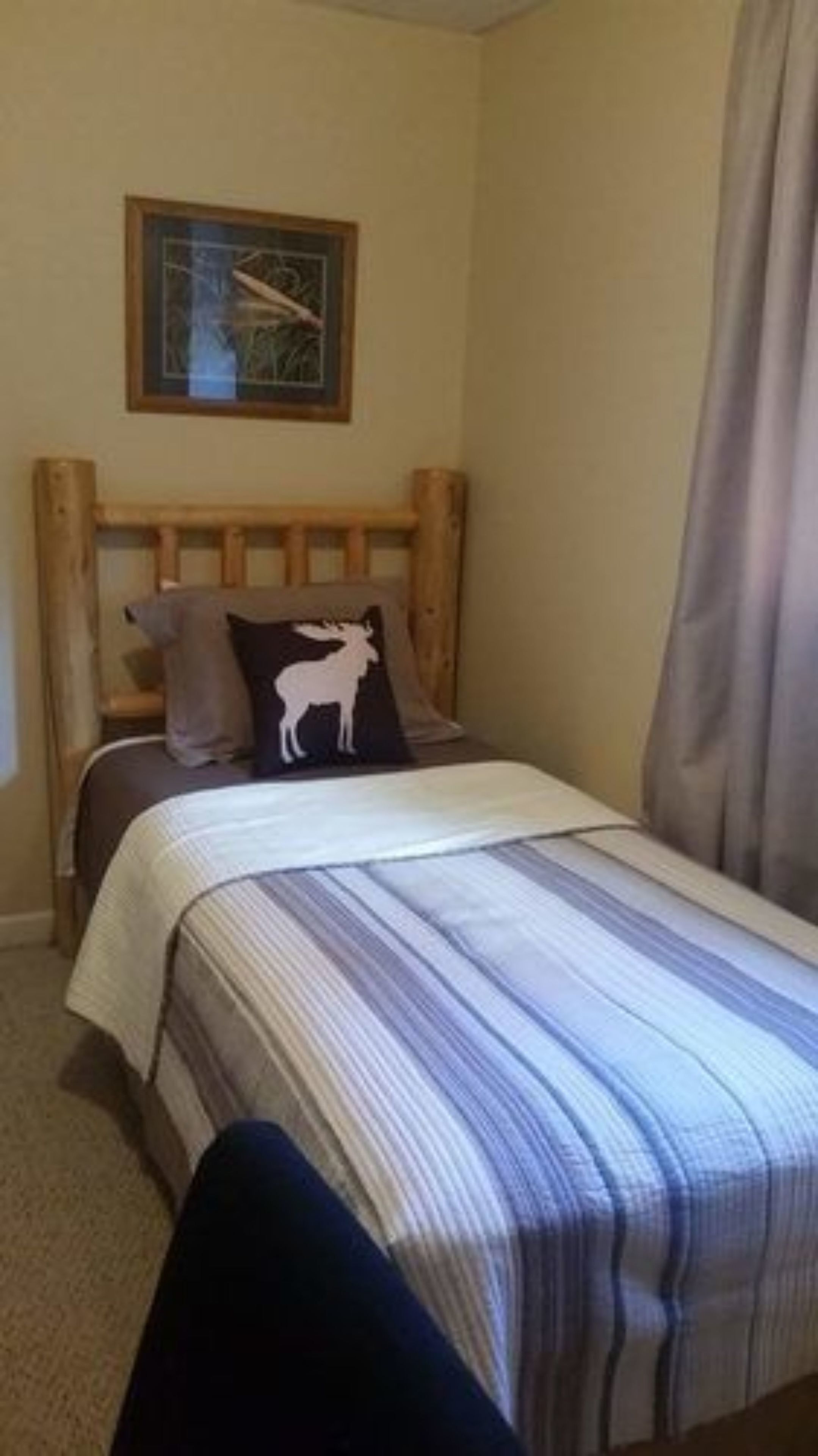 Ein Schlafzimmer mit einem hölzernen Kopfende, einem Bett mit gestreifter Bettwäsche, einem Kissen mit einem Hirschmotiv und einem gerahmten Bild an der Wand.