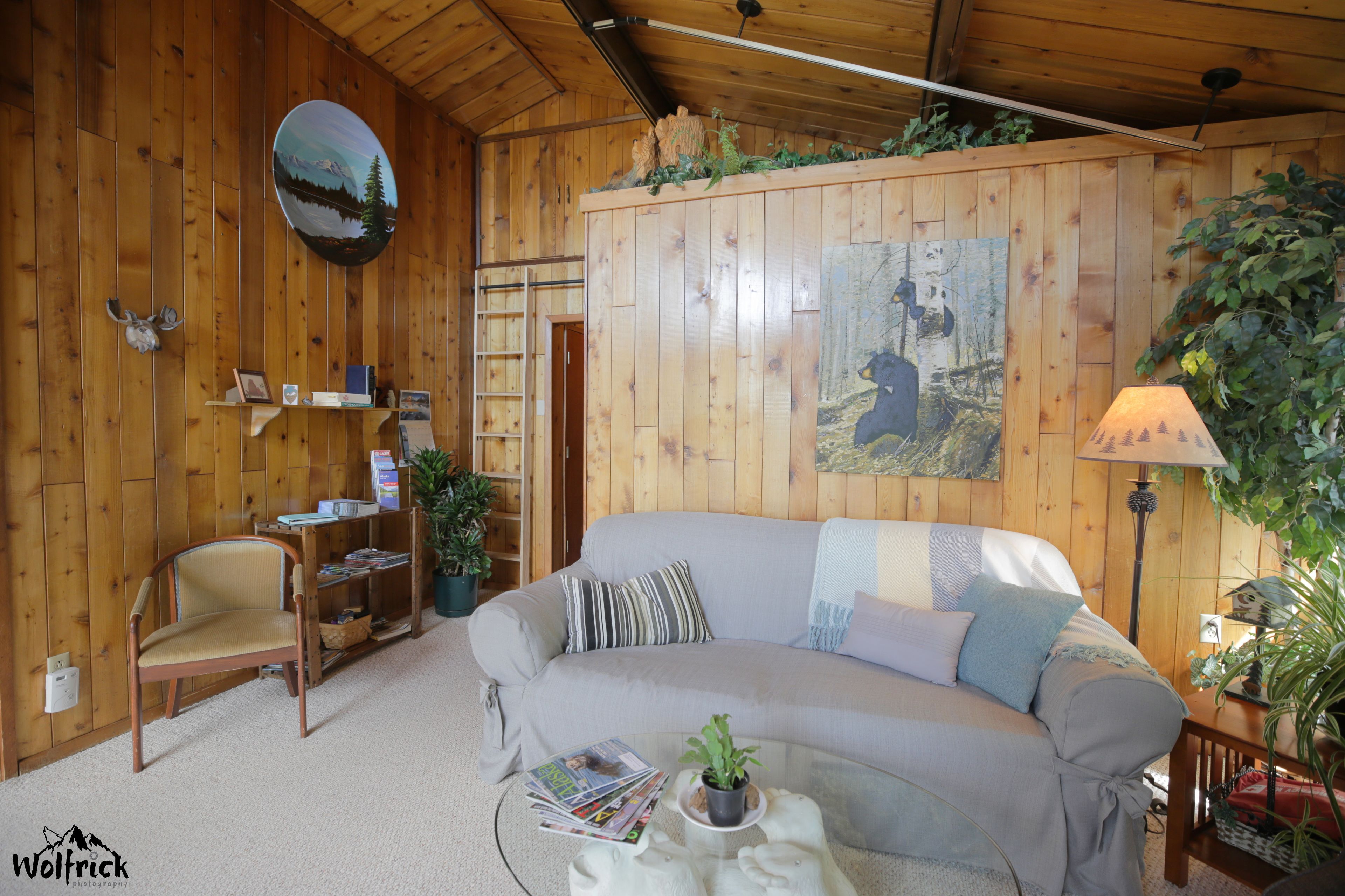 Ein gemütliches Blockhaus-Interieur mit Holzausstattung, einer Couch, einem Sessel, einem Couchtisch und einem Bücherregal.