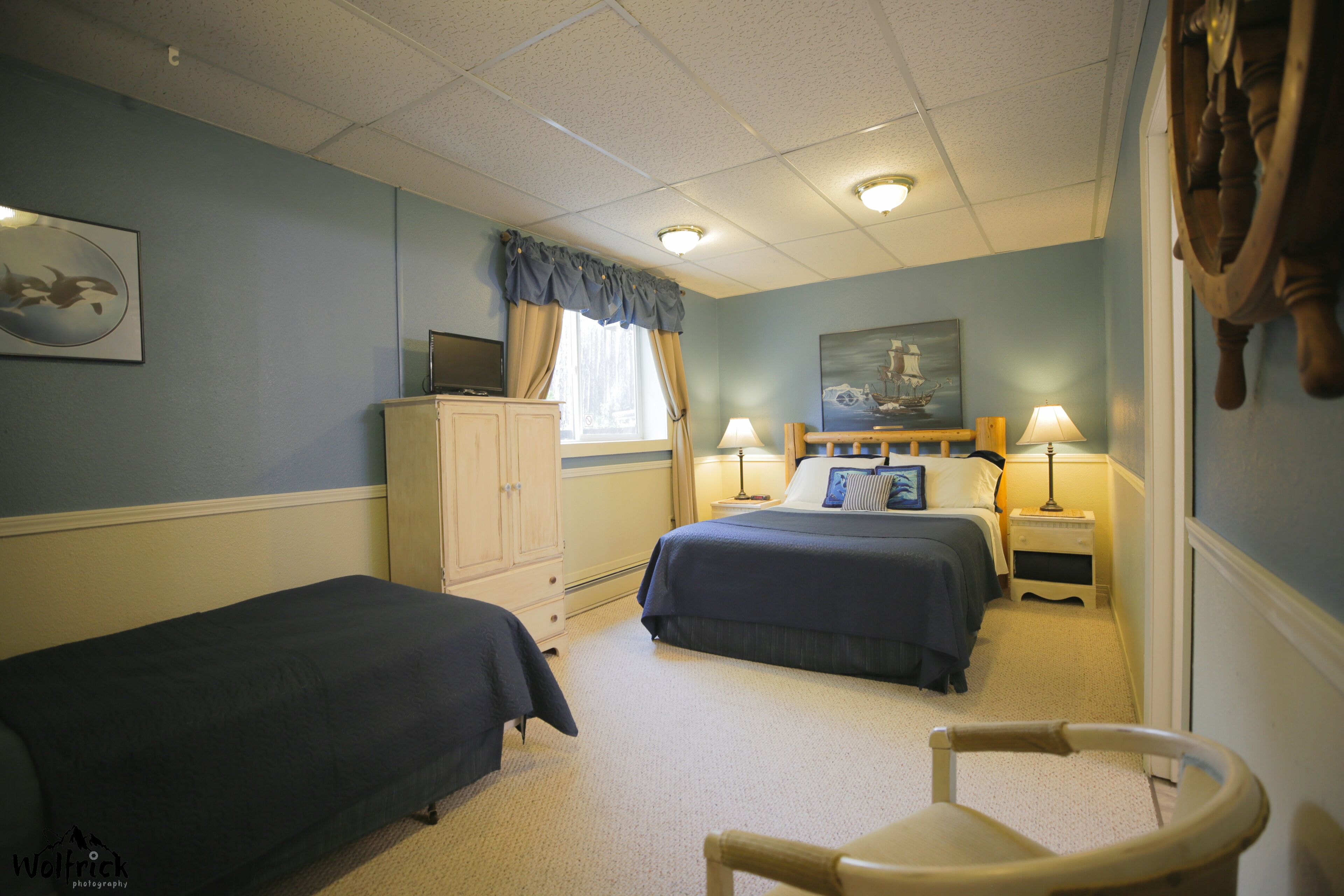 A bedroom with two beds, a desk, a chair, and a television.