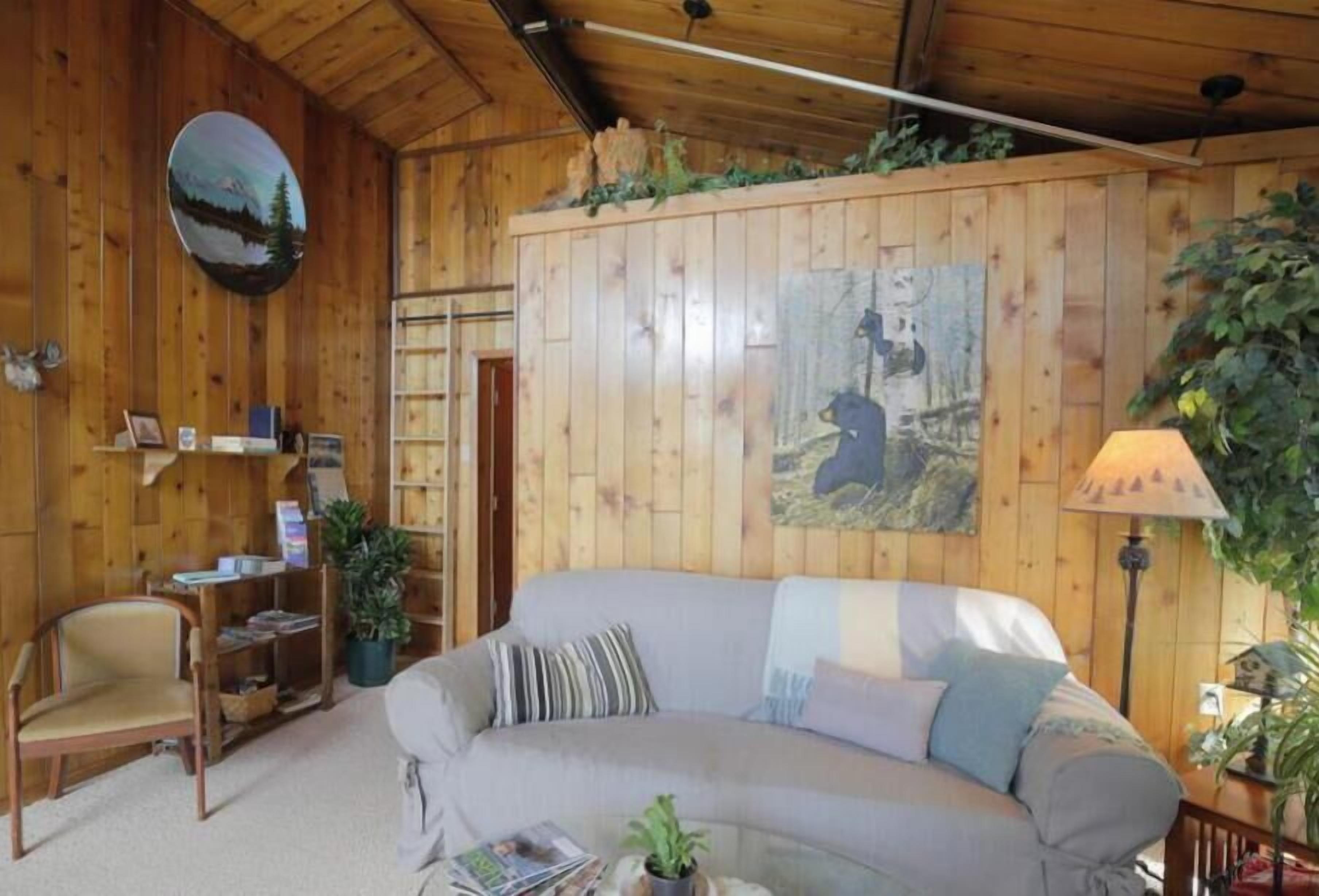 A cozy room with a wooden interior, a sofa, a chair, a lamp, and a painting on the wall.