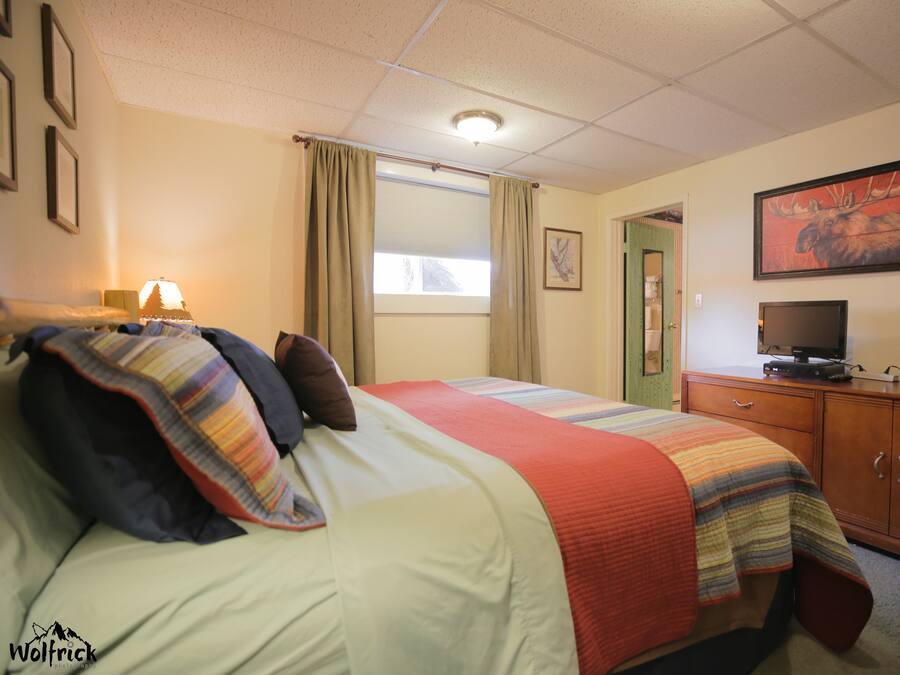 A hotel room with a bed, a television on a wooden cabinet, and a painting on the wall.