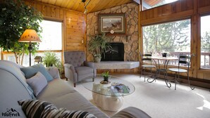 A cozy living room with a stone fireplace, a sofa, a coffee table, and a dining area with chairs and a table. - Jewel Lake Bed and Breakfast (Anchorage)