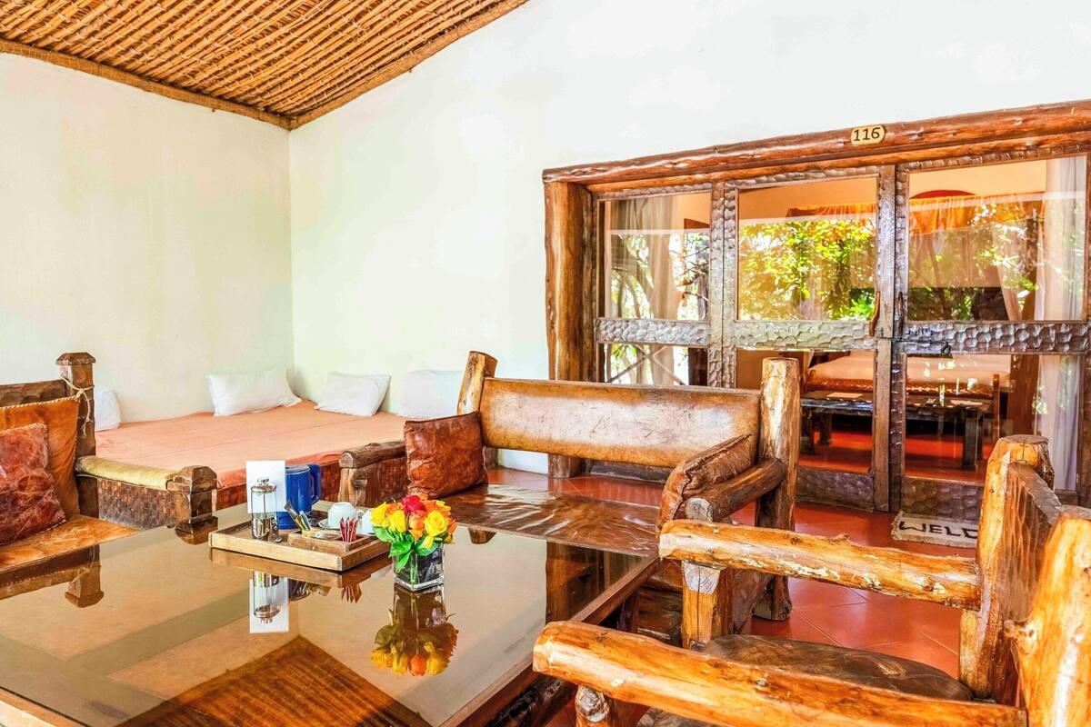 Un intérieur rustique en bois, avec une table en verre, des sièges en cuir et une vue sur l’extérieur par une fenêtre.